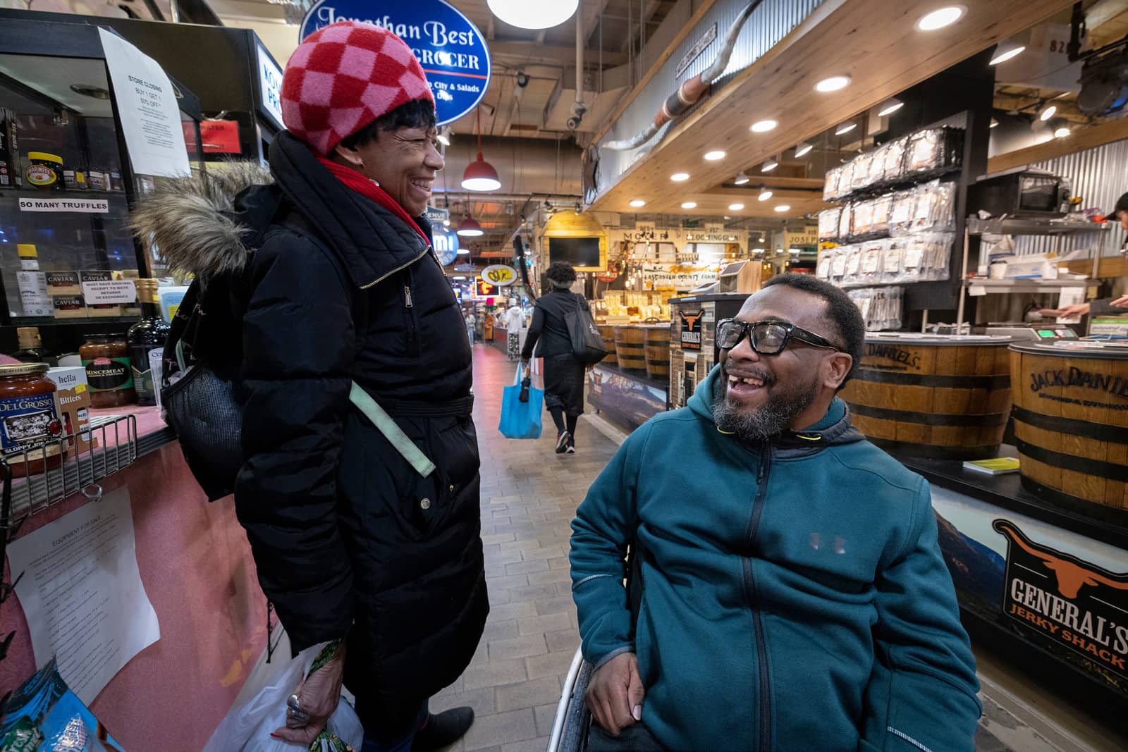 Rodney, a Black man using a wheelchair, laughs with another shopper in Reading Terminal Market