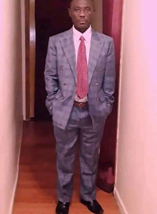 Asende, wearing a suit, stands in a hallway