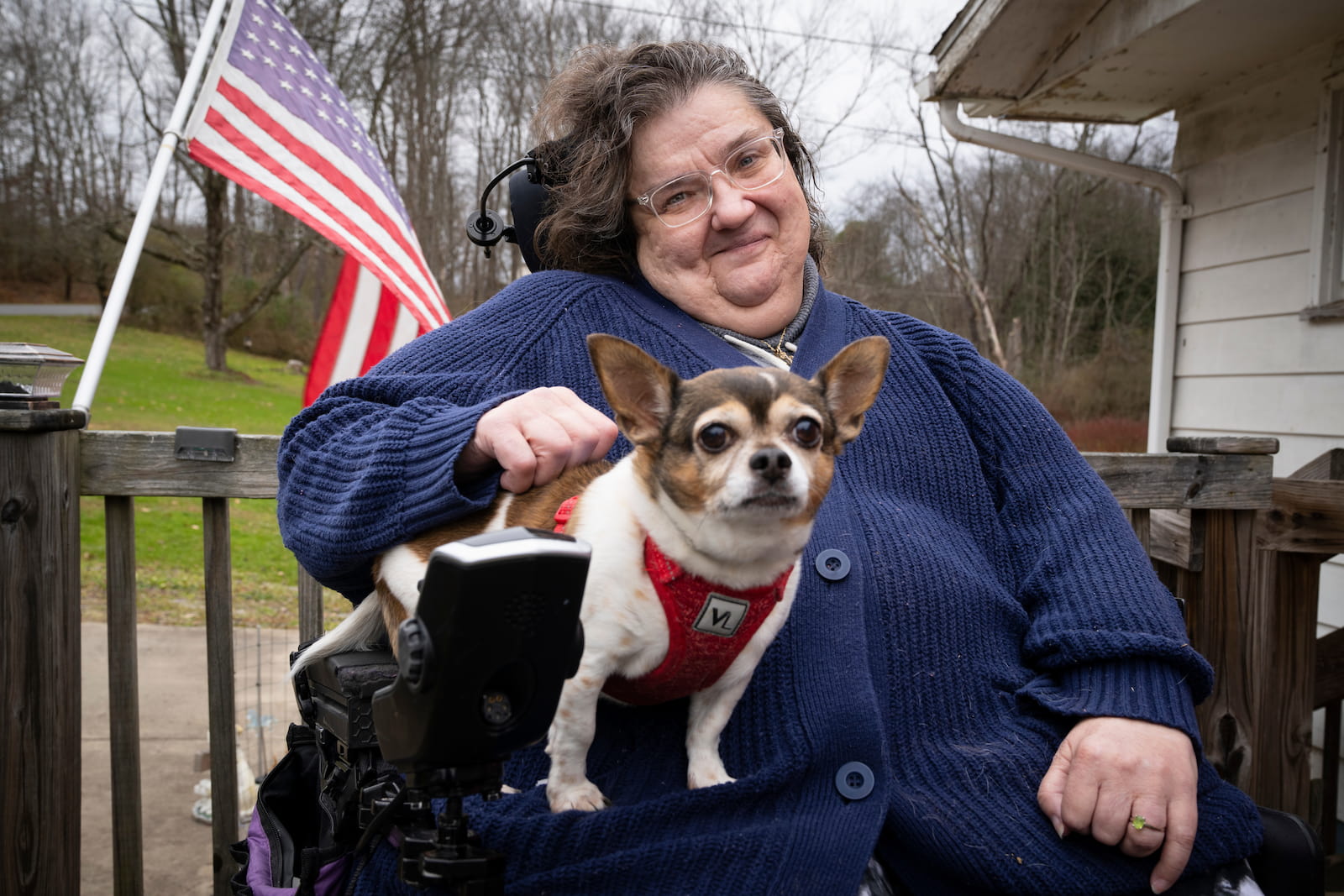 Cindy holding her dog on her lap outside her house, in front of a US flag