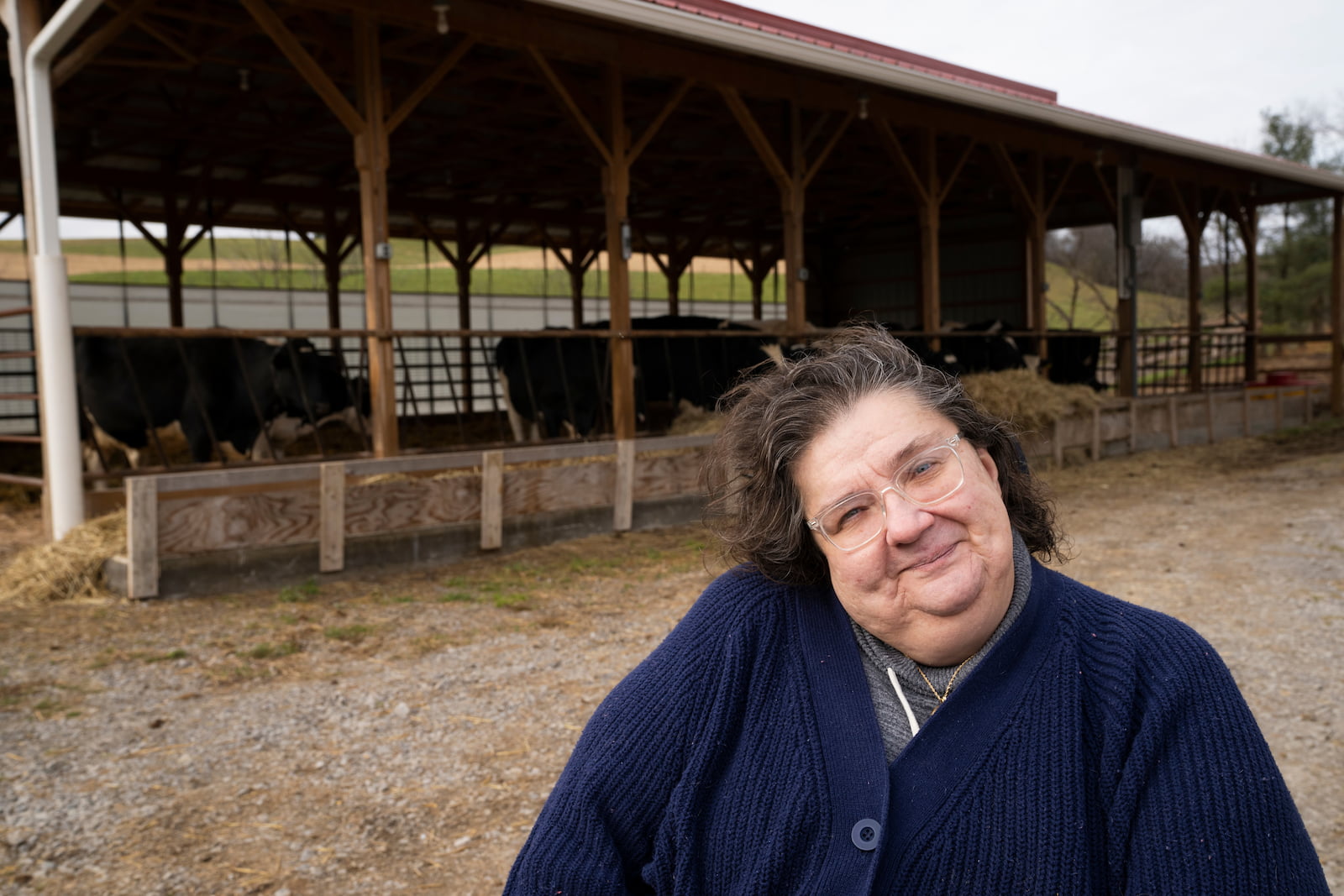 Cindy, smiling, outdoors near a cow shed