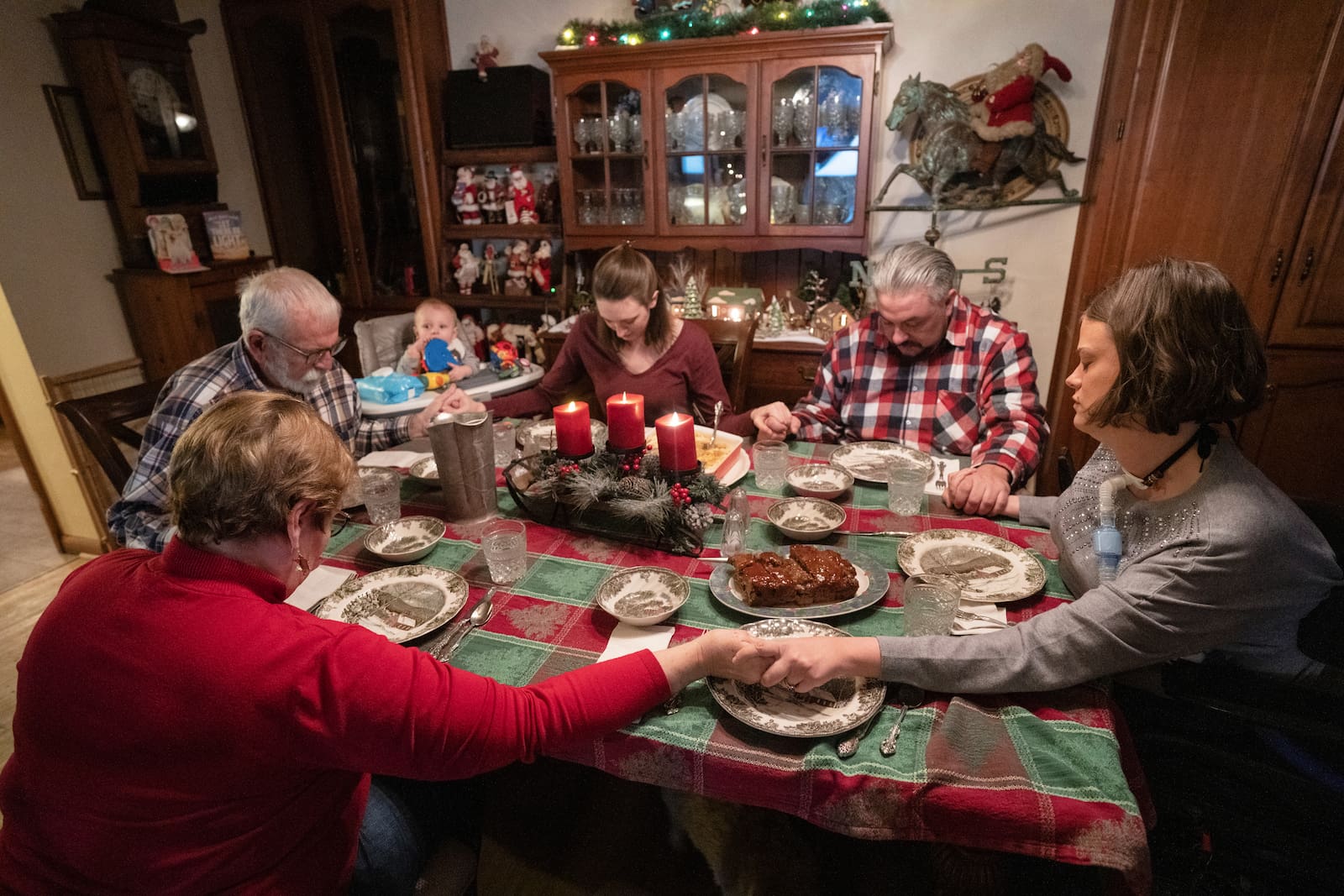 Josie and family around dinner table with Christmas decor holding hands to say grace