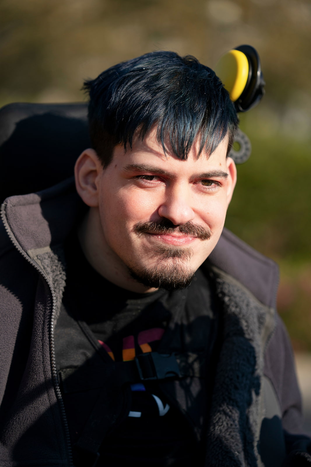 Mark, smiling determinedly from his wheelchair with attached head switch