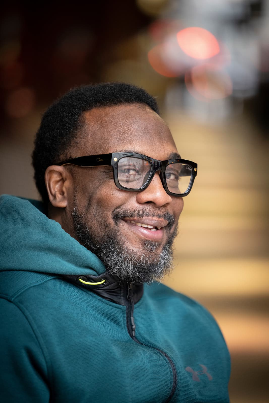 Rodney, with his black Ray-Ban style eyeglasses and salt and pepper beard and mustache, smiles for a close-up portrait