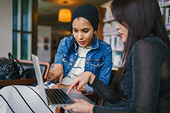 two women sitting together looking at a notebook computer