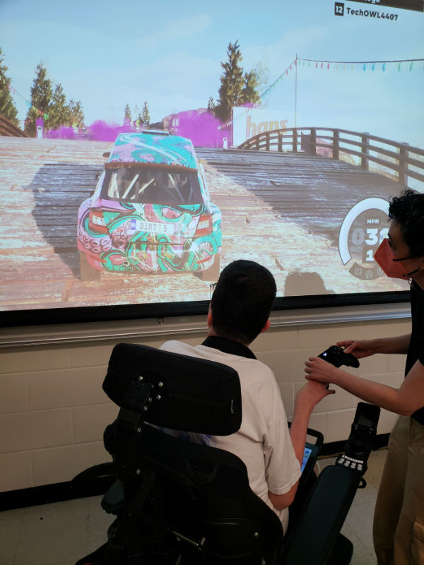 young adult student with teacher, learning use of adapted controller for xbox