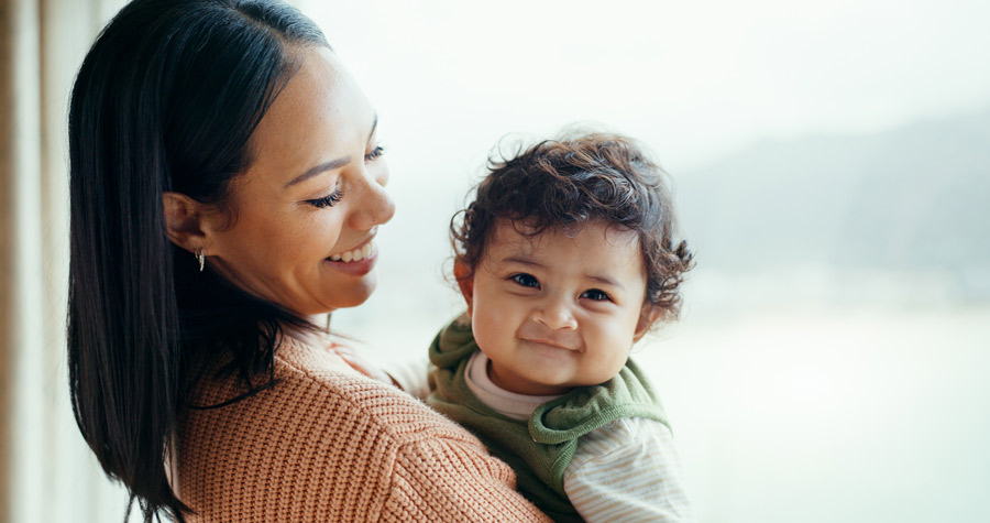 Smiling parent holds grinning baby in a light-filled area