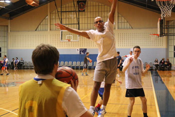 Nate leaps, arms extended while playing guard in an indoor basketball game