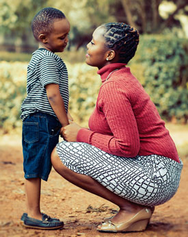 Woman squats facing little boy as they smile and hold hands