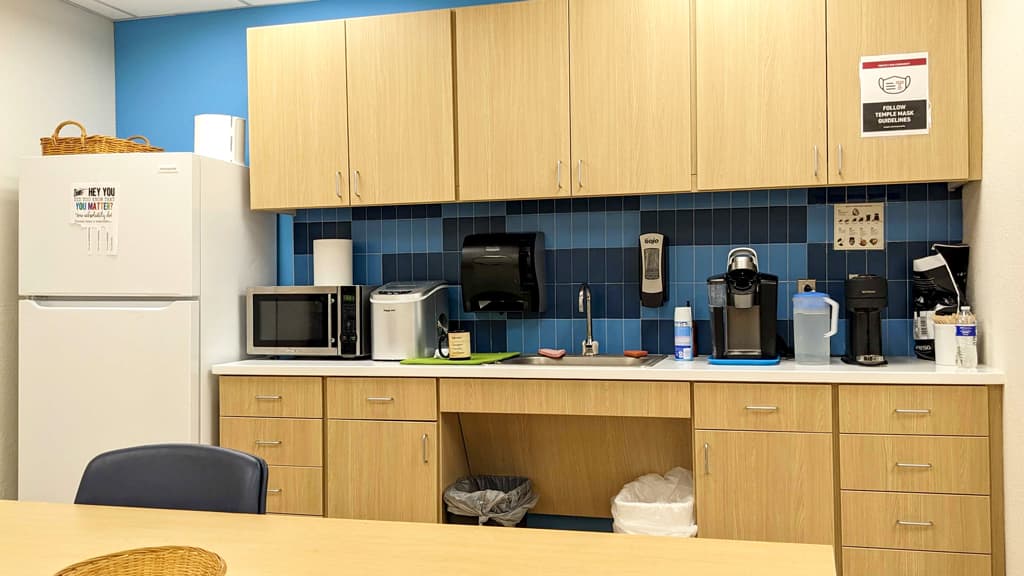Room with table, sink, counter, under-counter and wall cabinets, kitchen equipment, and blue-tiled wall