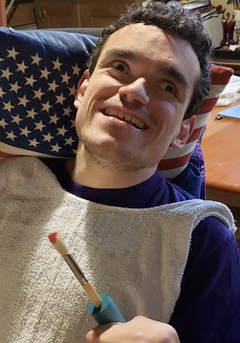 Robert smiles, has an American flag pillow in his wheelchair