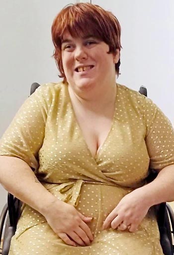 Shirley is smiling, wearing a wrap dress and using her wheelchair