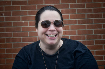 Tanya, smiling and wearing sunglasses, in front of a brick wall