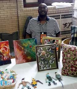 William sits at a table with hand-crafted items including clocks for sale