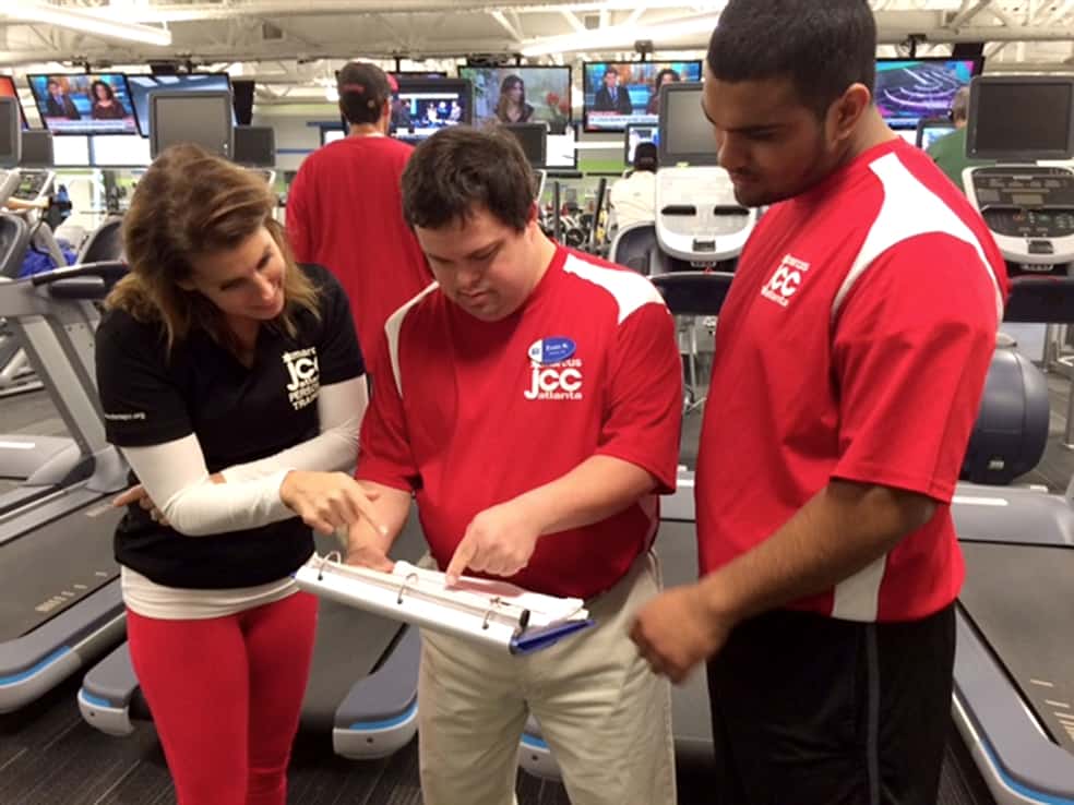 Three people in a gym wearing shirts with matching logos look at a clipboard together