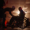 In silhouette, a person leans down to Fred, who is using a wheelchair