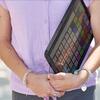 a student on campus holds their electronic tablet loaded with an AAC app for communication