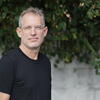 David Graber, wearing a dark t-shirt and eyeglasses, in an outdoor setting with plants
