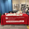 Table with Institute on Disabilities tablecloth is covered with IOD information sheets and giveaway items