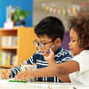 Two Pre-K or Kindergarten children of color side by side at table using pencils and paper