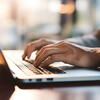 A person's hands typing on laptop keyboard at a table