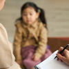 Adult writes in a notebook, facing a preschool-aged child and their parent