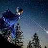 Woman in twirling garment in a night landscape before a starry sky with a bright shooting star