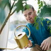 Young adult uses a watering can in a leafy setting