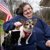 Cindy holding her dog on her lap outside her house where US flag flies on a railing