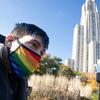 Close-up of Mark outdoors wearing a rainbow face mask with his AAC device in view and a tall building beyond