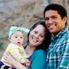 Two smiling parents pose outdoors with baby