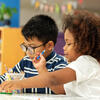 Two Pre-K or Kindergarten children of color side by side at table using pencils and paper