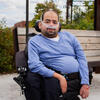 Jaggar DeMarco, a man using a power chair and breathing support, sits outdoors in a park setting