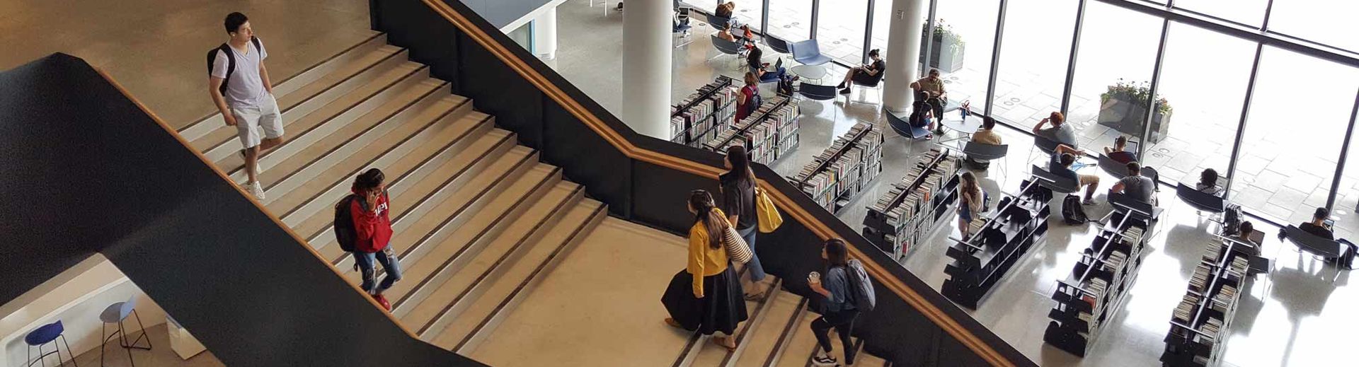 students and others moving through bright, open library space with staircase and soaring ceilings