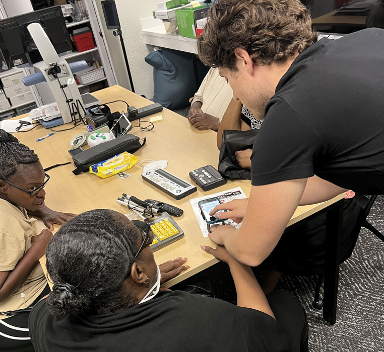 A staff member demonstrates assistive tech at a table with others